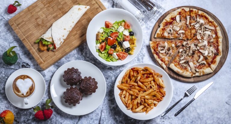 A delicious spread of food including pizza, pasta, salad, wrap, muffins, and coffee.